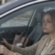 Młoda kobieta siedzi w samochodzie na firmowym parkingu i nie wysiada, patrzy przed siebie przez szybę