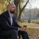 Mężczyzna w garniturze siedzi rano na ławce w parku z kawą na wynos i spokojnie patrzy przed siebie