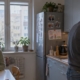 Napięty mężczyzna stoi przy kuchennym blacie, a jego żona siedzi nieruchomo przy stole; na krześle wisi różowy plecak