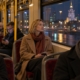 Młoda kobieta w wieczornym tramwaju patrzy przez okno na światła miasta, a pozostali pasażerowie wpatrują się w telefony